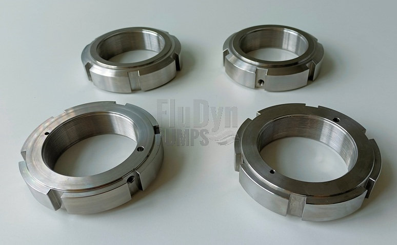 Vier Spannmuttern aus Metall liegen nebeneinander auf einem neutralen weißen Hintergrund. Zwei liegen auf ihrer Oberseite, die anderen zwei auf der Unterseite. Außen kann man Einkerbungen zum Spannen und innen eine Aussparung für eine Nut sehen.